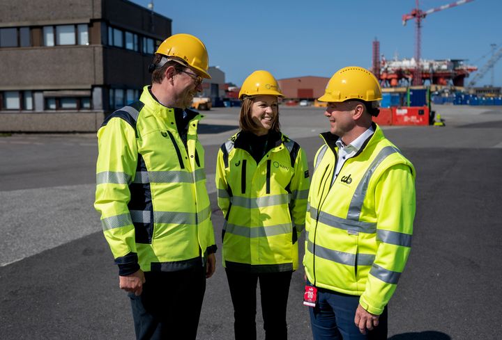 En%20kvinne%20og%20to%20menn%20i%20gul%20vernejakke%20og%20hjelm%20inne%20p%E5%20et%20industriomr%E5det.